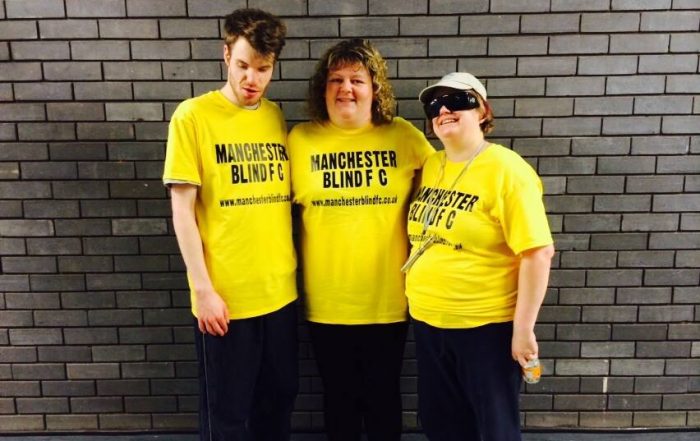 Helen Lawson stood on the right along with two friends in yellow t-shirts in front of a grey brick wall.