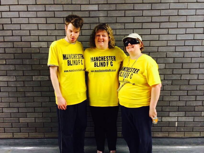 Helen Lawson stood on the right along with two friends in yellow t-shirts in front of a grey brick wall.