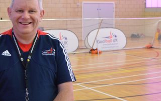 Robert Avery stood in a Goalball UK referee's top in front of a goalball goal.