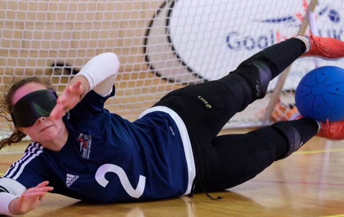 Antonia Bunyan in a GB shirt saving a goalball shot with her legs.