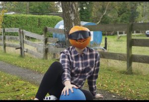Samantha Gough wearing a chequered shirt laying in a goalball defensive position with a pumpkin on her head!