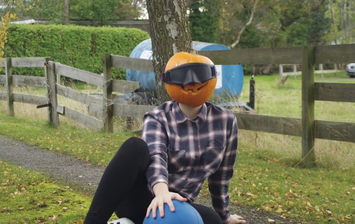 Samantha Gough wearing a chequered shirt laying in a goalball defensive position with a pumpkin on her head!