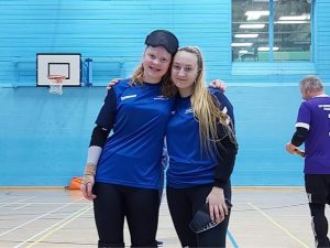 Chelsea Hudson & Samantha Gough stood together in their Goalball Academy tops whilst stood together in a sports hall.