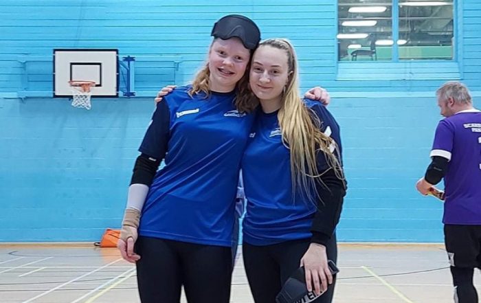 Chelsea Hudson & Samantha Gough stood together in their Goalball Academy tops whilst stood together in a sports hall.