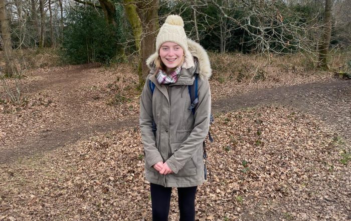 Phoebe stood on a woodland trail with a big coat and fluffy hat.