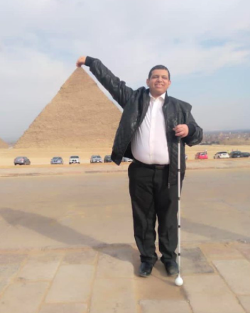 Khalil in front of a pyramid in Egypt! Khalil is doing a pinching action with the top of the pyramid in the background, impressive!