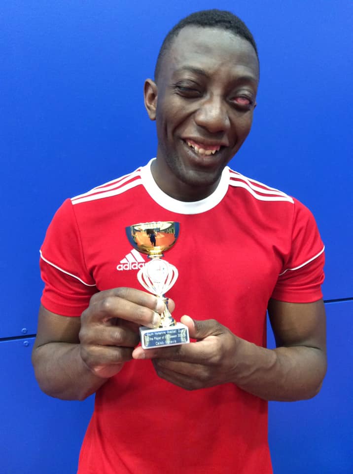 Caleb Nanevie in a bright red shirt holding a small trophy with a big smile!