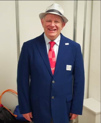 Robert Avery standing in his navy blue Tokyo 2020 suit with a red tie and a big smile!