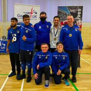 Birmingham team with coaches and players huddled together in front of a Goalball UK banner with their gold medals.