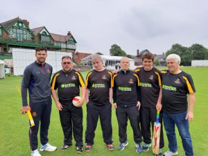 An image featuring 5 cricket players in black playing shirts, who are stood next to a coach.