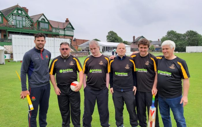 An image featuring 5 cricket players in black playing shirts, who are stood next to a coach.