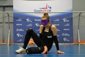 Ciara McDonagh on a goalball court in a ready position whilst wearing purple eyeshades.