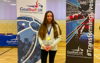 Ciara stood wearing her well earned Player of the day medal in front of two Goalball UK banners.