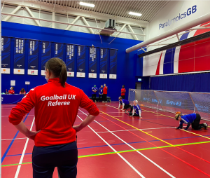 Faye Dale refeering a goalball game with Cambridge Dons in view on the right side of court.