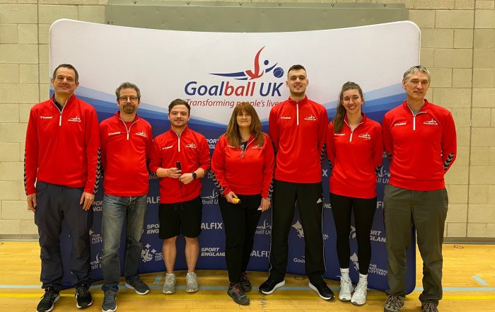 The 7 new Referees in their Goalball UK red fleeces in front of a Goalball UK banner. Left to right: Matthew Exley, Craig Meulen, Aaron Mitchell, Louise Gough, Stephen Reilly, Anna Martin, and Stuart Tapp.