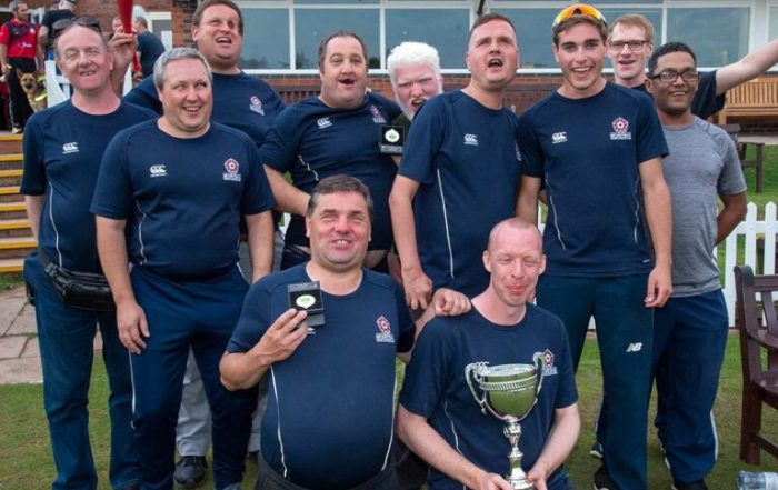 A group of people stood together at a blind cricket event, all players are wearing navy blue shirts and someone is holding a trophy!