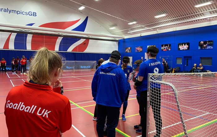 Sophie Blagg wearing a red Goalball UK jacket whilst goal judging, listening in on Birmingham time out tactics.