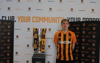 Adam standing in front of the EFL League 1 trophy wearing his amber and black Hull City shirt after the Tigers were crowned 2021 champions.