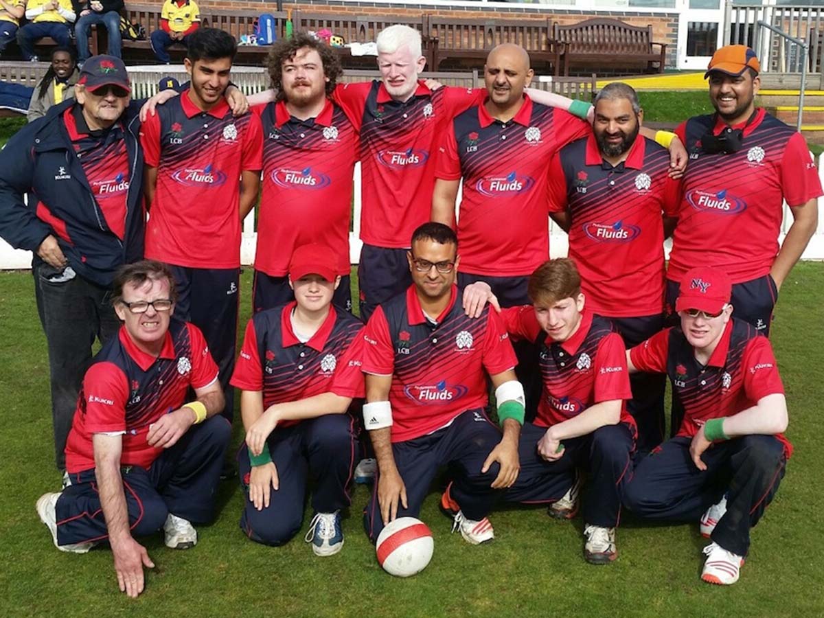 A Lancashire Lions VI cricket team photo of everyone in their red and navy blue shirts, some wearing camps with the sun shining down!