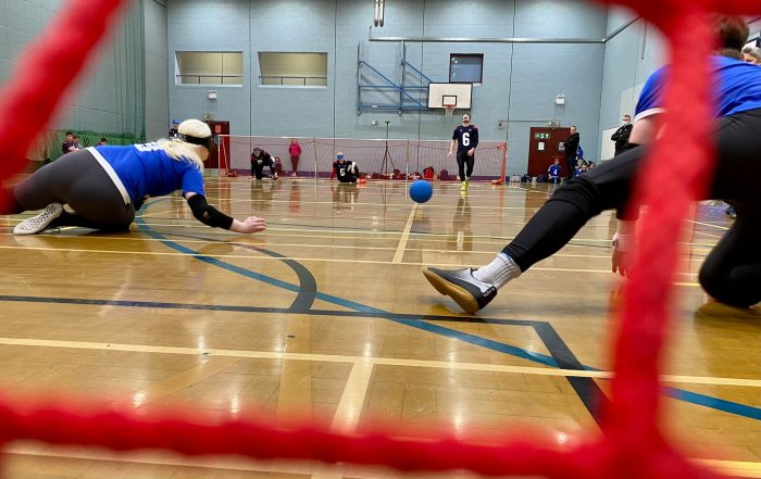 Cambridge gown diving to save an oncoming shot from George Williams of RNC. The photo is taken from behind the net, with some of the net in view.