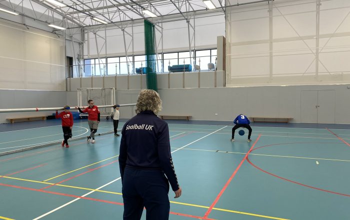 Kathryn Fielding in navy blue Goalball UK tracksuit onlooking a young goalball player attempting a Brazilian goalball throw!