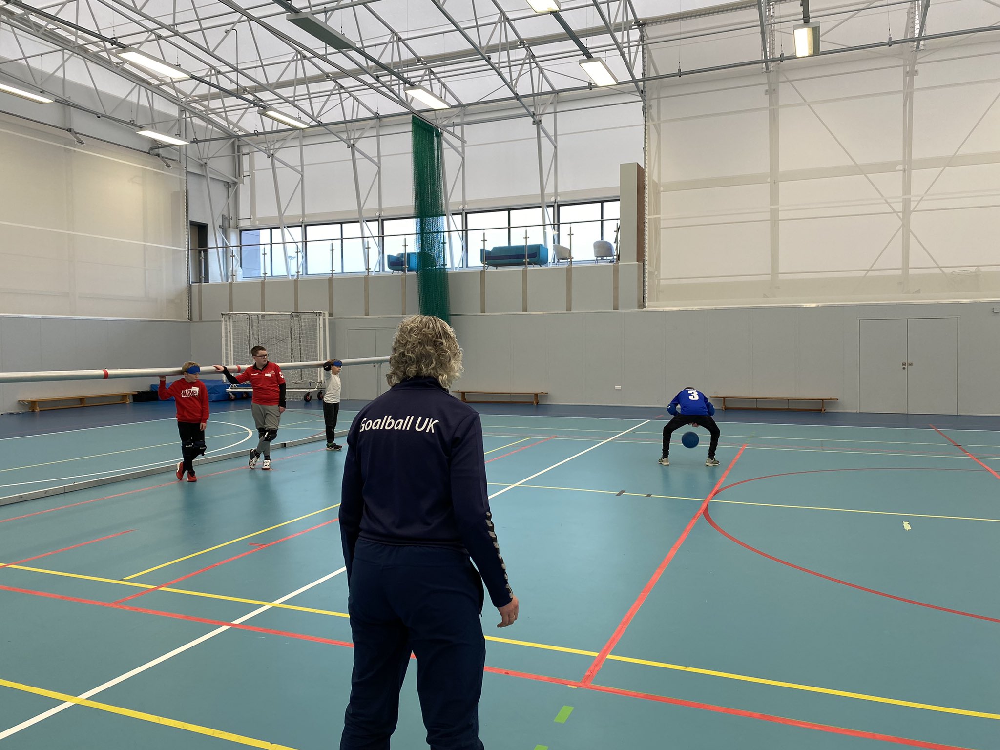 Kathryn Fielding in navy blue Goalball UK tracksuit onlooking a young goalball player attempting a Brazilian goalball throw!