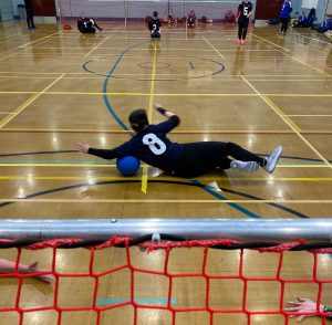 Freya Gavin of RNC Hereford diving to save a shot, wearing the number 8 jersey in the centre of court.