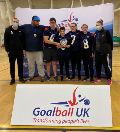 RNC Academy players holding the Novice Shield with the Goalball UK board in front of them.