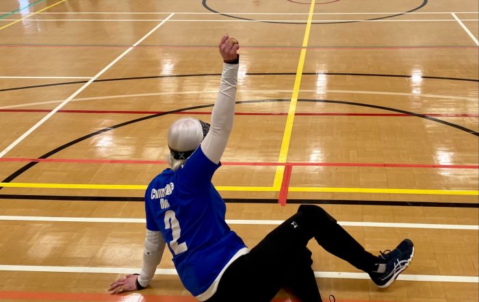 Sarah Leiter on court in centre position wearing the number 2 shirt for Cambridge Dons.Sarah has her hand raised to the sky in celebration after scoring a goal!