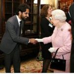Ameen Memon shaking hands with the Queen, Ameen is smiling proudly in a nice suit, as the queen is wearing a light pink dress.
