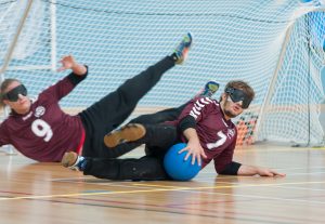 Dan Blast on court in the 2018 Goalfix Cup wearing Maroon jerseys with white numbers. The centre player has saved a goalball with his left winger diving behind him.
