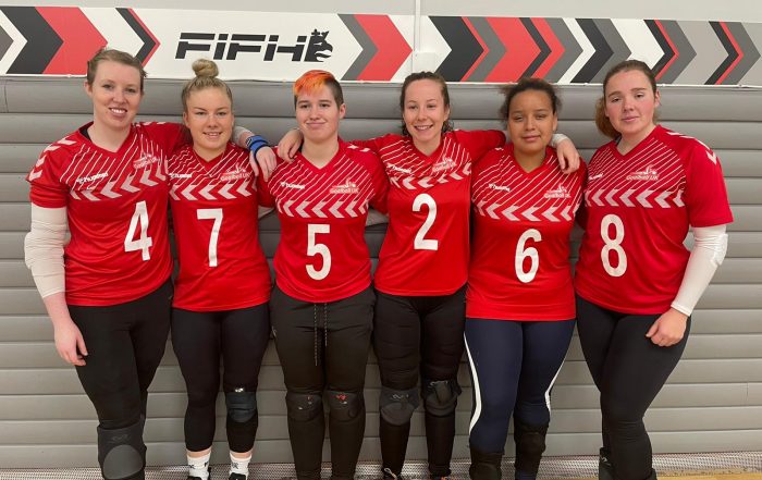 GB Womens squad standing together with all 6 players having their arms around one another. They're all wearing their red hummel GB jerseys.