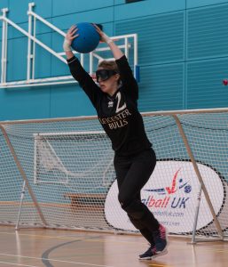 Georgie Bullen playing for Leicester Bulls at a past Goalfix Cup. Georgie is in the motion of throwing a goalball whilst wearing a black Leicester Bulls jersey.