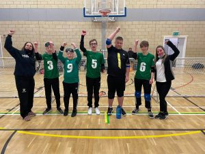 Nottinghamshire Sheriffs novice team with 5 players and 2 coaches with their arms in the air after a competition. Everyone has got smiles on their faces after a great day.