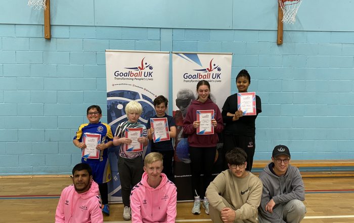 A group photo of people at our Manchester Junior Day, with 5 players standing with certificates with volunteers sitting below them.