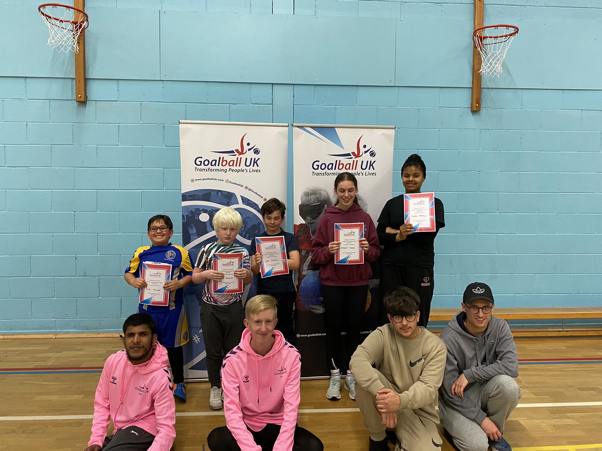 A group photo of people at our Manchester Junior Day, with 5 players standing with certificates with volunteers sitting below them.