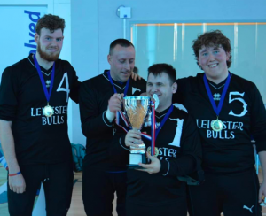 Leicester Bulls team photo after they won a competition. 4 players are in the photo with their medals and black jerseys. The player second from the right is holding the trophy, that is almost as big as him!