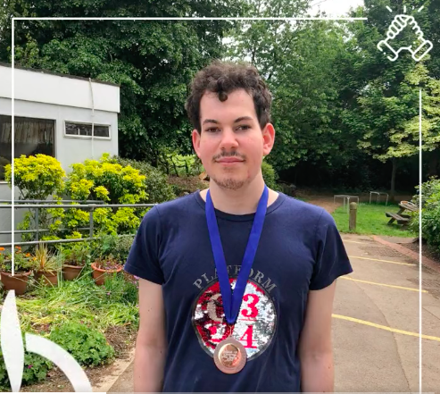 Edwin of Winchester Goalball Club standing on a path at his college, wearing his bronze medal he and his team won at the recent novice tournament.