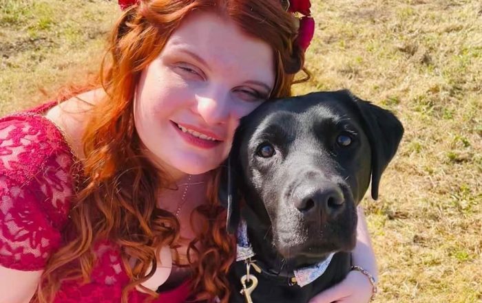 Abbie-Rose hugging her black Labrador guide dog Evie Abbie is wearing a red dress.