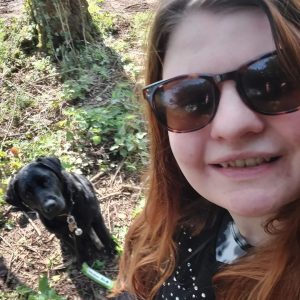 Abbie and Evie taking a selfie In a forest. Abbie's face is in the right corner and the camera is angled towards the ground where Evie is looking up.