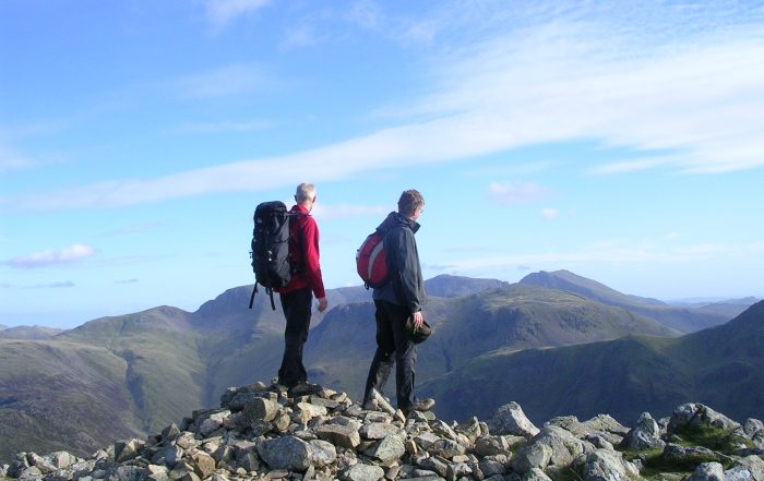 Andrew and his dad Mike on a mountain walk in the Lake District. They have just got to the peak of one of the mountains, with bright blue sky in the distance.