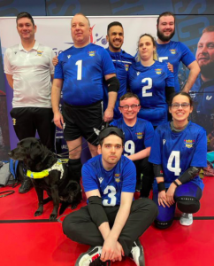 Birmingham Intermediate Trophy team photo with players and coaches standing together in their blue jerseys. Guide dog Pippen has joined the photo as a big part of the team!