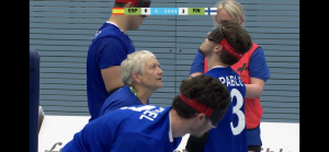 A screenshot of the European Para Youth Games livestream in the game between Spain and Finland. Judith Oakley is refereeing and is checking a Spain players eyeshades at a substitution.