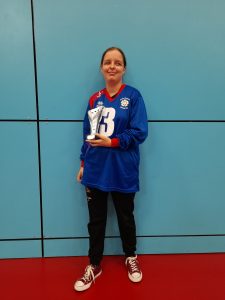 Klaudia Orzel standing in a blue South Yorkshire goalball jersey, and black tracksuit bottoms holding a silver trophy.