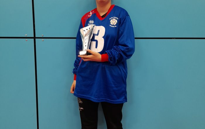 Klaudia Orzel standing in a blue South Yorkshire goalball jersey, and black tracksuit bottoms holding a silver trophy.