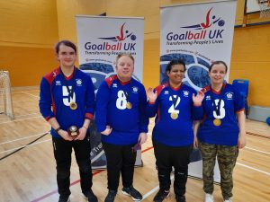 South Yorkshire novice team photo as the team have just won gold at a novice tournament! All 4 players are wearing blue South Yorkshire jerseys, and standing in front of two Goalball UK pop up banners.