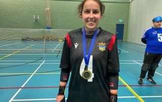Laura Brooks wearing a black Birmingham jersey, wearing a Player of the Day medal she won at an Intermediate South Matchday! Laura is smiling proudly to the camera.