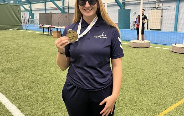 Samantha Gough holding her bronze medal from the European Para Youth Games, whilst wearing her navy blue Great Britain polo shirt.