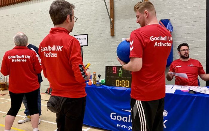 An activator holding the goalball as a referee inspects it