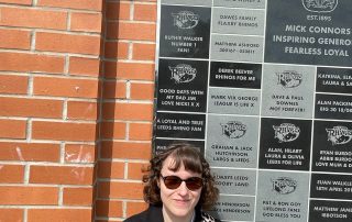 Ella stood infront of the Leeds Rhinos sign. Ella is wearing sunglasses and has a leopard print back strap.